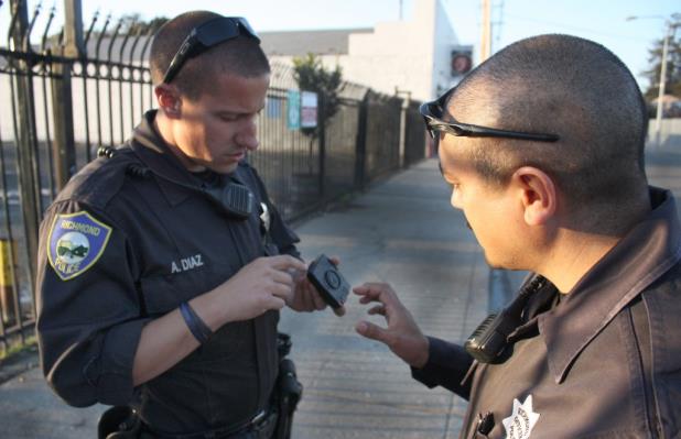 Richmond Police Officer Anthony Diaz, left, looks at fellow officer Phillip Sanchez's body camera. Sanchez, right, is one of four officers selected to test body cameras for the department before they issue them to all patrol officers. (Photo by: Kevin N. Hume)